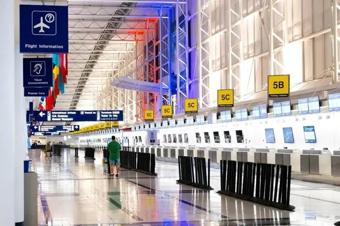 Traveler walking through a quiet airport terminal past check-in counters and flight information signs.