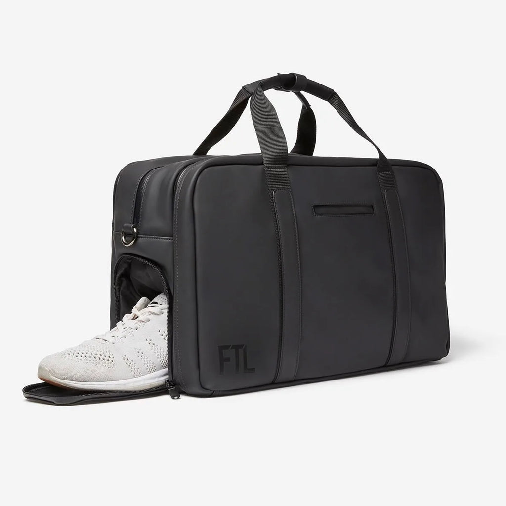 Black FTL gym duffel bag with side shoe compartment holding white sneakers.