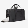 Black FTL gym duffel bag with side shoe compartment holding white sneakers.