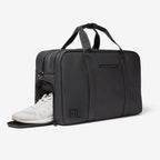Black FTL gym duffel bag with side shoe compartment holding white sneakers.