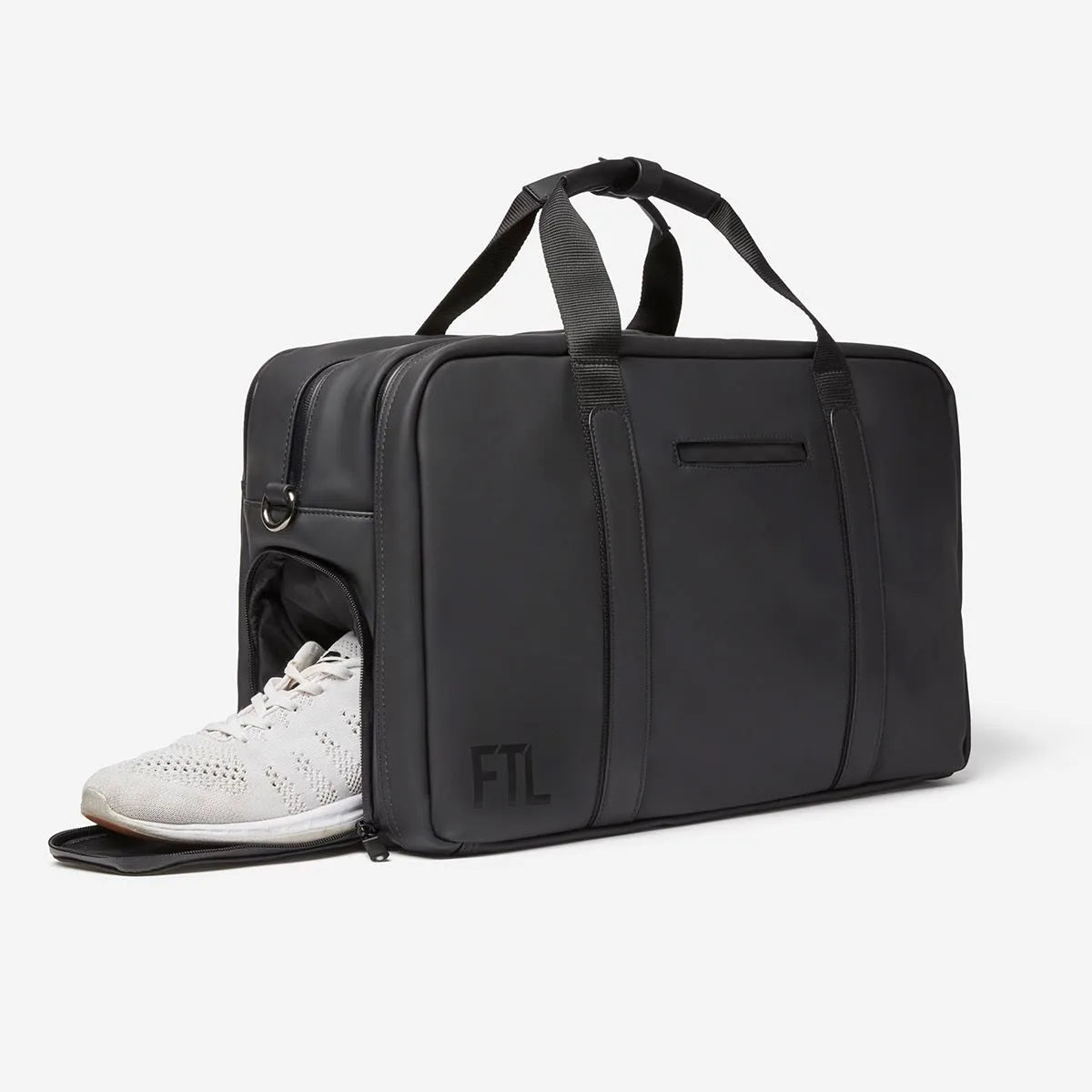 Black FTL gym duffel bag with side shoe compartment holding white sneakers.