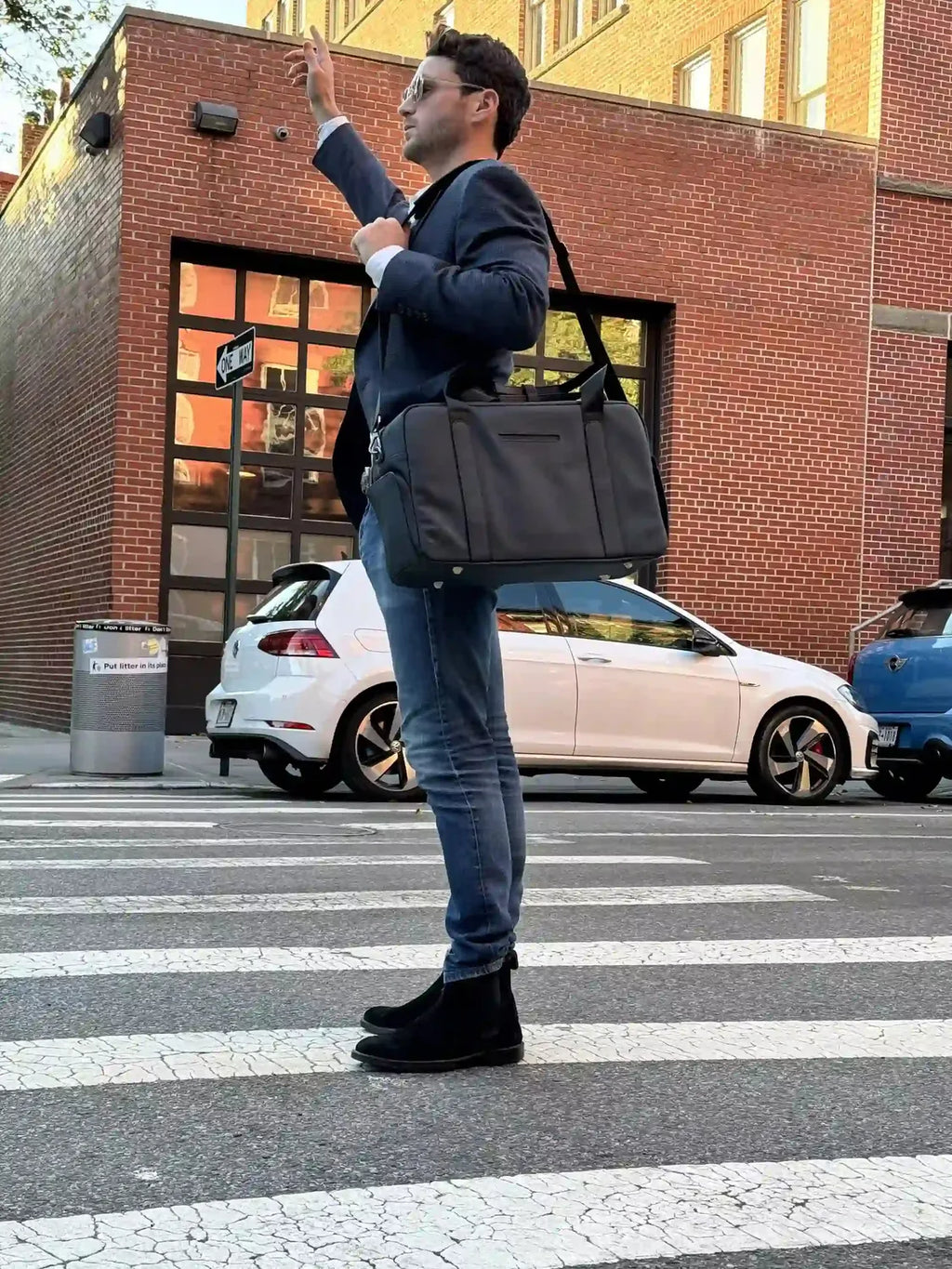 Person in blazer hailing a cab with a grey work duffel bag on a city crosswalk.