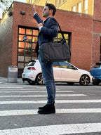 Person in blazer hailing a cab with a grey work duffel bag on a city crosswalk.